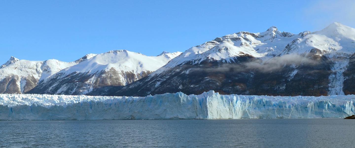 Glacier at the ocean's edge with snow capped mountains in the background