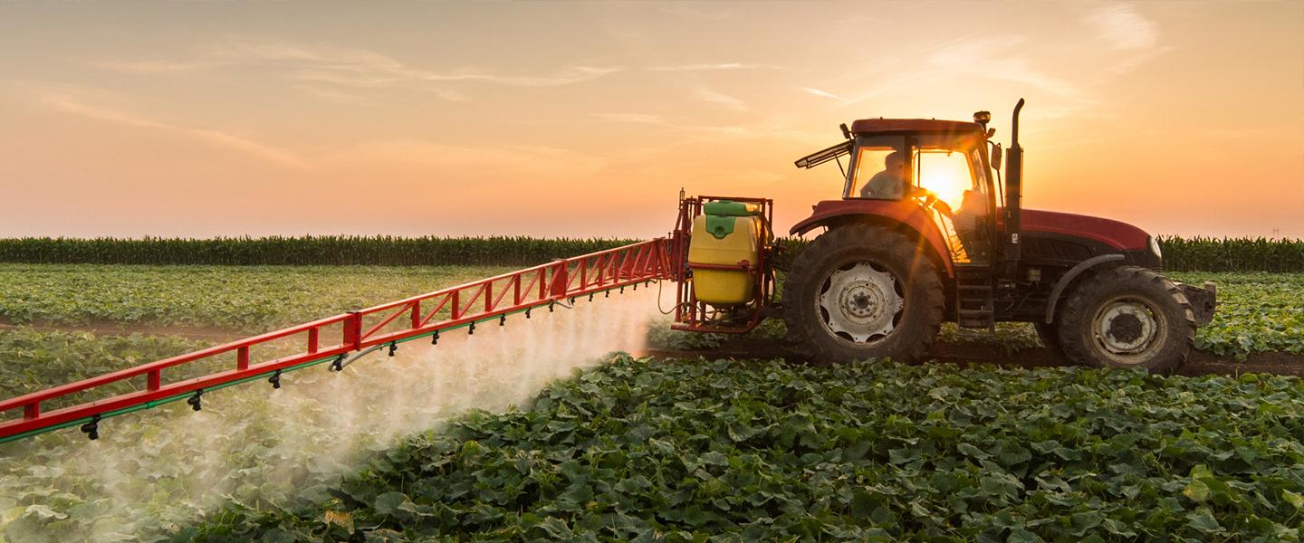 Commercial tractor spraying pesticides over crops