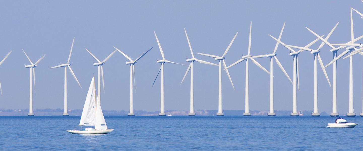 Wind farm in the ocean on a beautiful day with a sailboat in the foreground