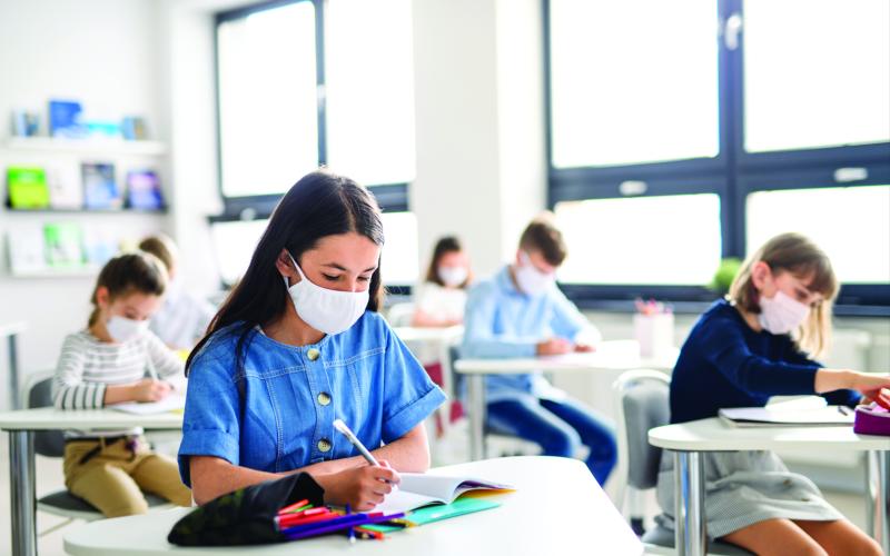 School kids in a classroom seated at desks wearing masks