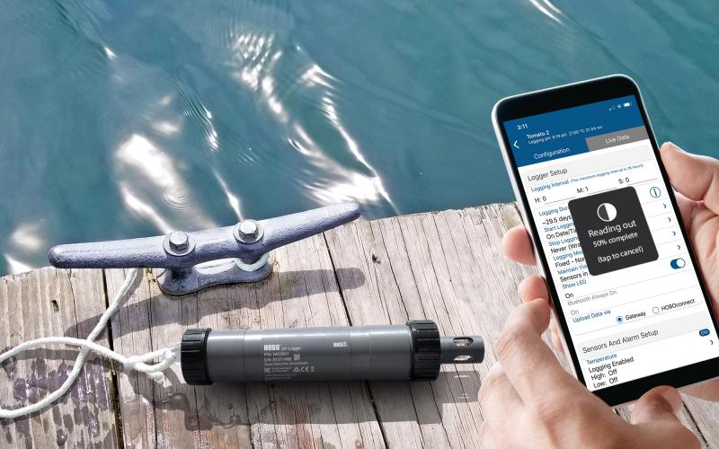 HOBO MX2500 on a dock with a phone being held in the forefront displaying the data