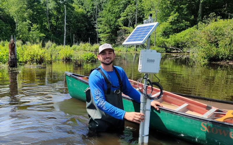 man standing in water next to canoe and monitoring system