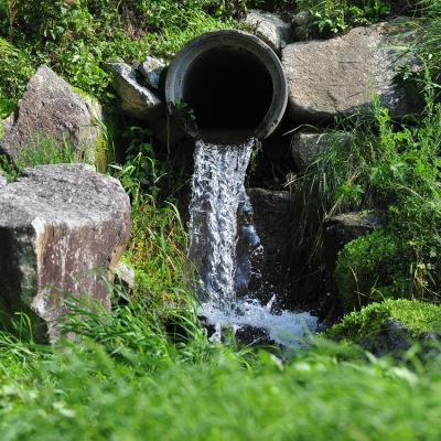 A rocky area with water draining out of a large concrete pipe.