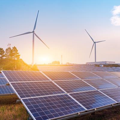 A sunrise or sunset with windmills in the background and solar panels in the foreground.