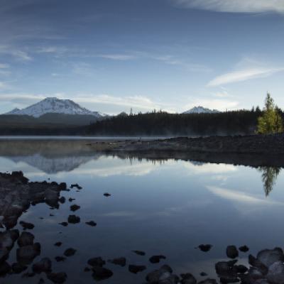 mountain lake with rocky shore reflects trees and sky